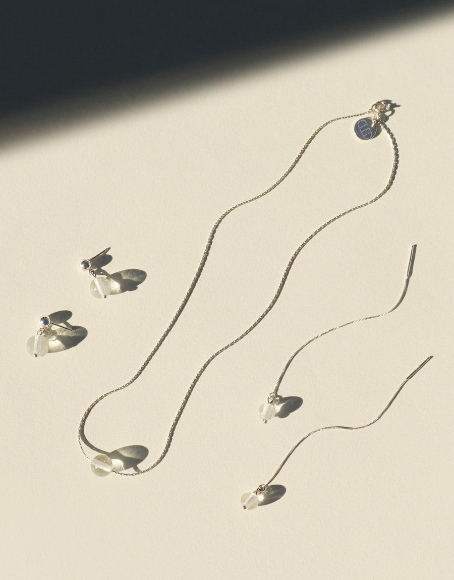 A collection of eco-conscious necklaces and earrings by CLED, featuring silver chains, clear beads, and clear stones, crafted from repurposed glass.