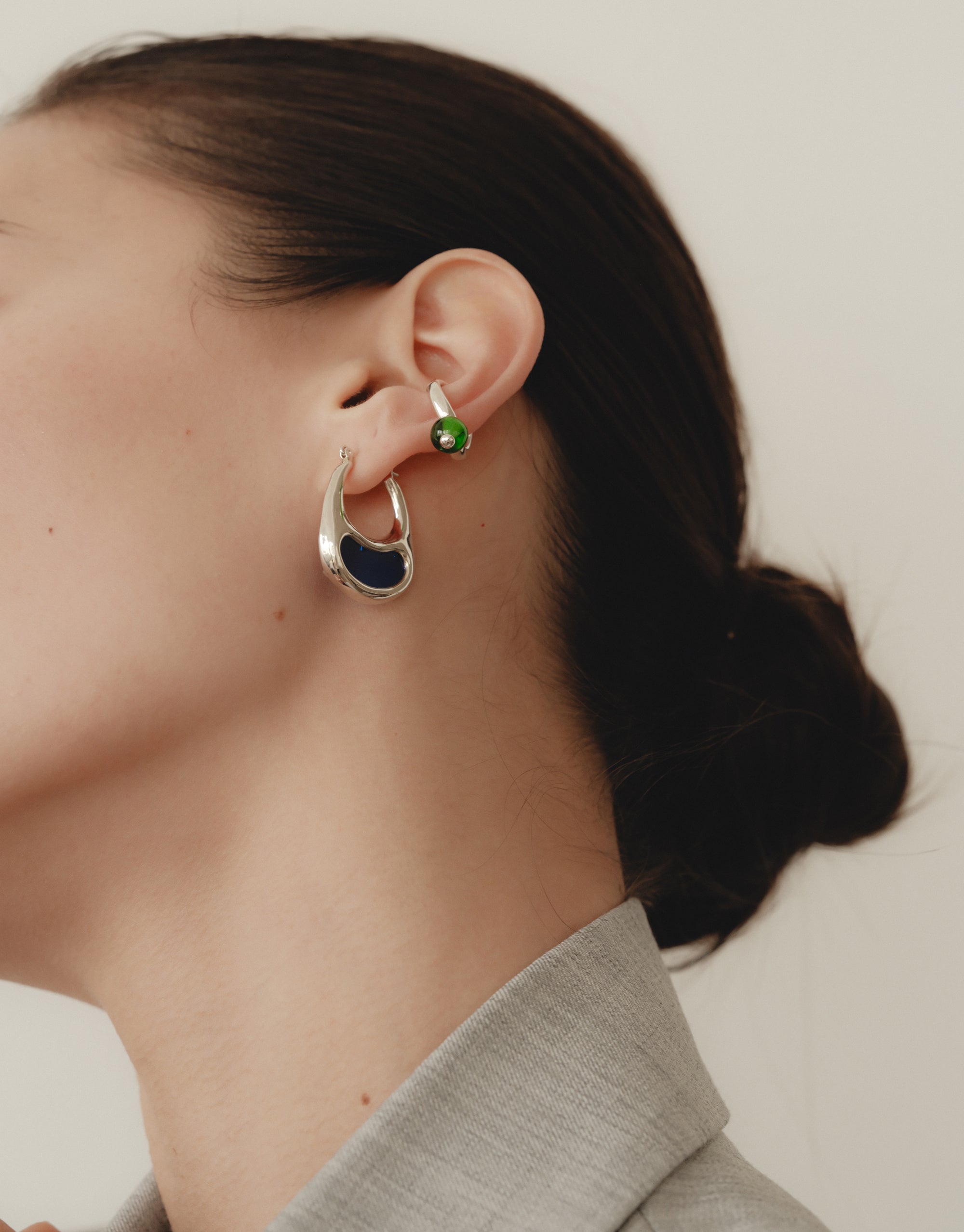 Elegant Bean Hoop Earrings | Large showcased on a model's ear, featuring a sleek curved design inspired by nature's organic shapes. The earrings embody growth and transformation, reflecting the beauty of legumes. A perfect accessory for those who appreciate nature-inspired jewelry. CLED