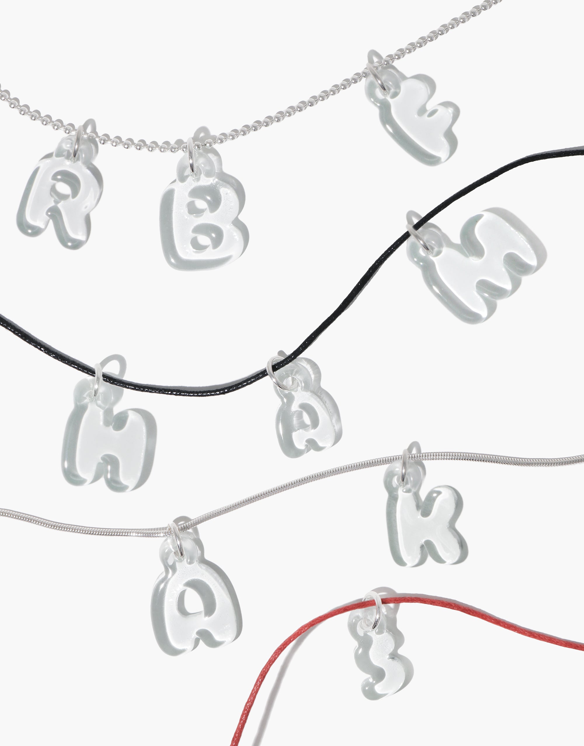 Silver ball chain necklaces with various letter and number charms displayed on different colored cords, showcasing versatile styling options for the Ball Chain Necklace. Adjustable length for personalized wear, perfect for adding custom charms. CLED